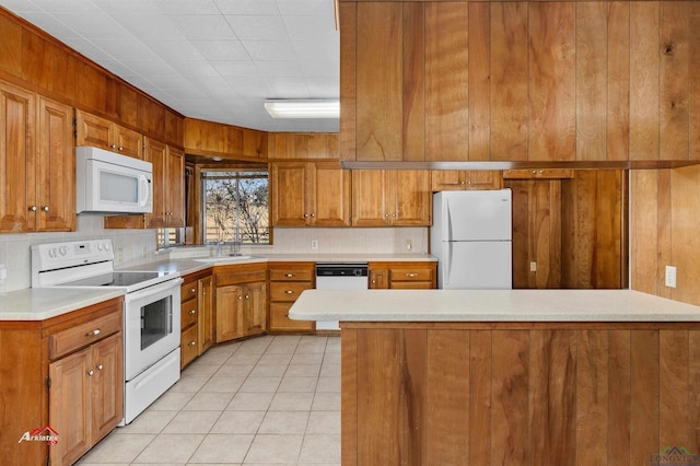 kitchen featuring sink, backsplash, wood walls, white appliances, and light tile patterned floors