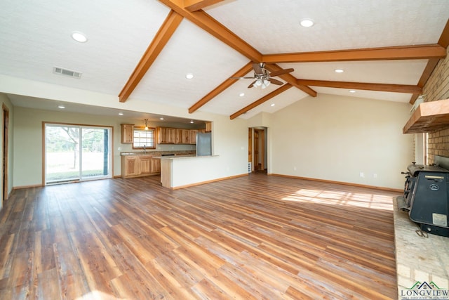 unfurnished living room with a wood stove, lofted ceiling with beams, ceiling fan, a textured ceiling, and light hardwood / wood-style floors