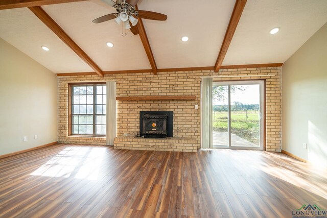 unfurnished living room featuring brick wall, ceiling fan, dark wood-type flooring, lofted ceiling with beams, and a wood stove