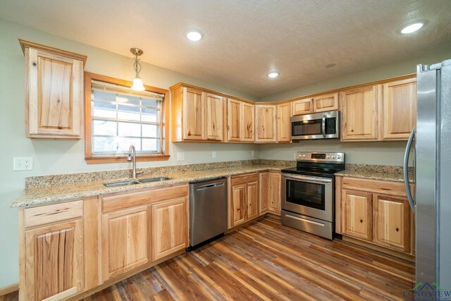 kitchen with pendant lighting, dark wood-type flooring, sink, light stone counters, and stainless steel appliances