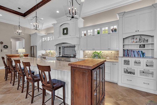 kitchen featuring stainless steel fridge, a kitchen island with sink, hanging light fixtures, white cabinetry, and light stone counters