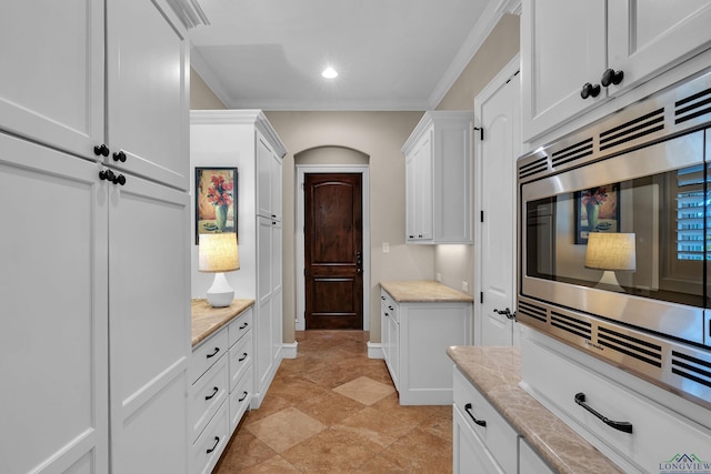 kitchen featuring stainless steel microwave, ornamental molding, white cabinets, and light tile patterned flooring