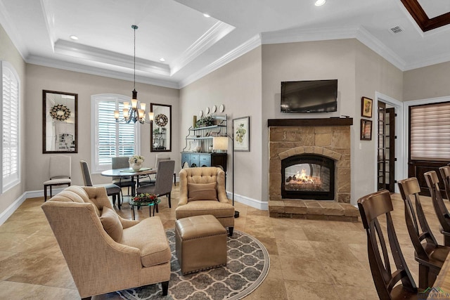 living room with crown molding, a stone fireplace, a chandelier, and a tray ceiling