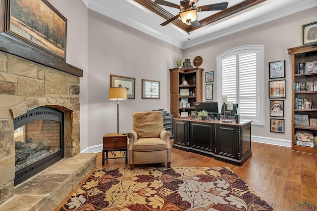 office area featuring a fireplace, ornamental molding, ceiling fan, a raised ceiling, and light wood-type flooring