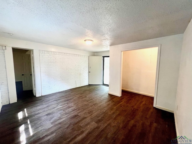 spare room featuring a textured ceiling, dark wood-type flooring, and brick wall