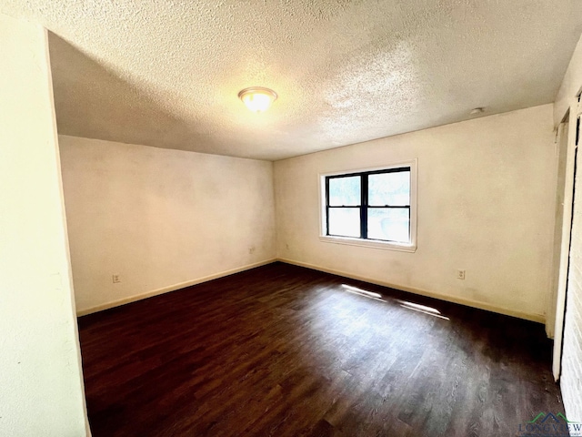 spare room featuring a textured ceiling and dark hardwood / wood-style floors