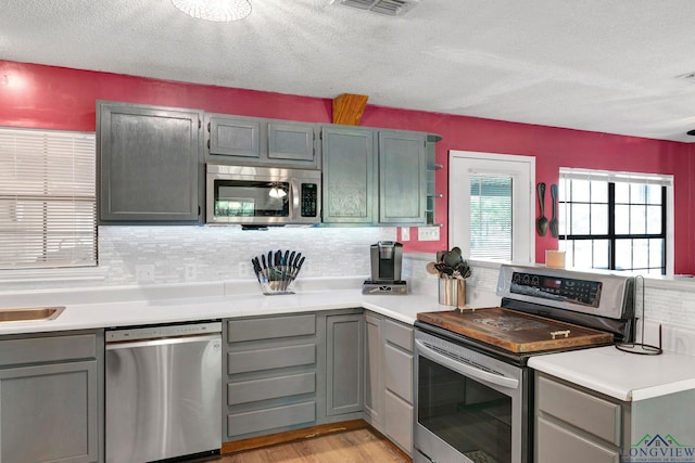 kitchen featuring a textured ceiling, light hardwood / wood-style floors, stainless steel appliances, and tasteful backsplash