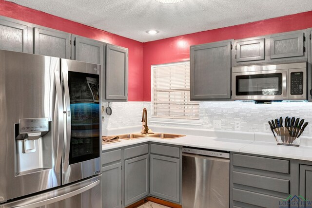 kitchen featuring decorative backsplash, gray cabinetry, a textured ceiling, stainless steel appliances, and sink