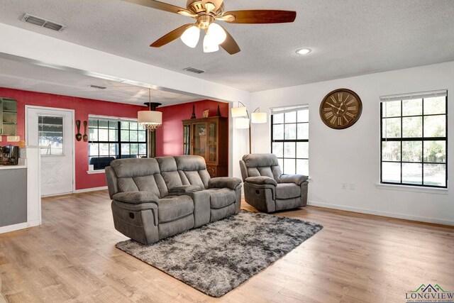 living room featuring ceiling fan, plenty of natural light, a textured ceiling, and light wood-type flooring