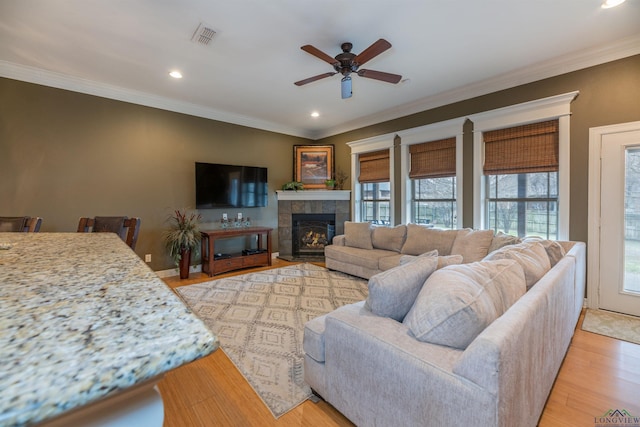 living room featuring a tiled fireplace, crown molding, ceiling fan, and light hardwood / wood-style flooring