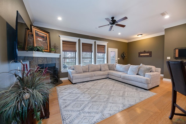 living room featuring crown molding, ceiling fan, a fireplace, and light wood-type flooring