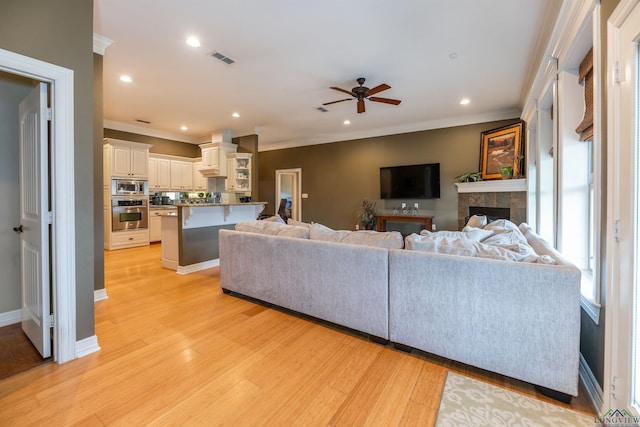 living room with ceiling fan, crown molding, a fireplace, and light wood-type flooring