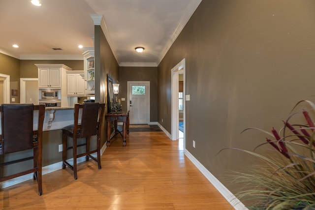 kitchen featuring a breakfast bar, white cabinetry, stainless steel microwave, ornamental molding, and light hardwood / wood-style floors