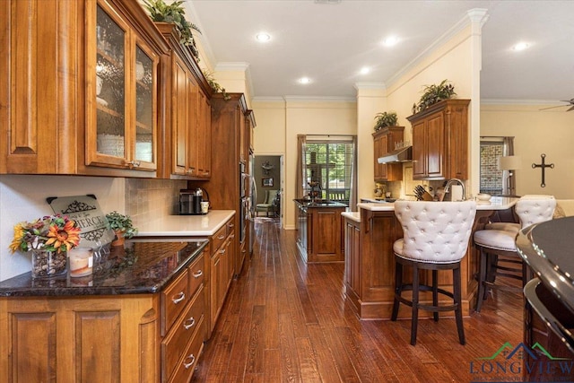 909 University Dr, Carthage, TX 75633 - kitchen featuring brown cabinets, dark wood finished floors, backsplash, glass insert cabinets, and under cabinet range hood
