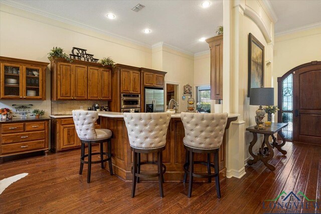 909 University Dr, Carthage, TX 75633 - kitchen with appliances with stainless steel finishes, brown cabinets, dark wood-style floors, glass insert cabinets, and crown molding