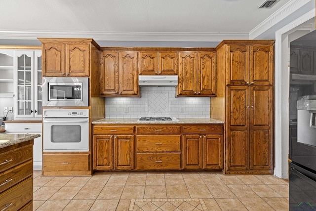 kitchen with light tile patterned floors, stainless steel appliances, backsplash, ornamental molding, and light stone counters