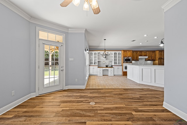 unfurnished living room featuring ceiling fan with notable chandelier, crown molding, and light wood-type flooring