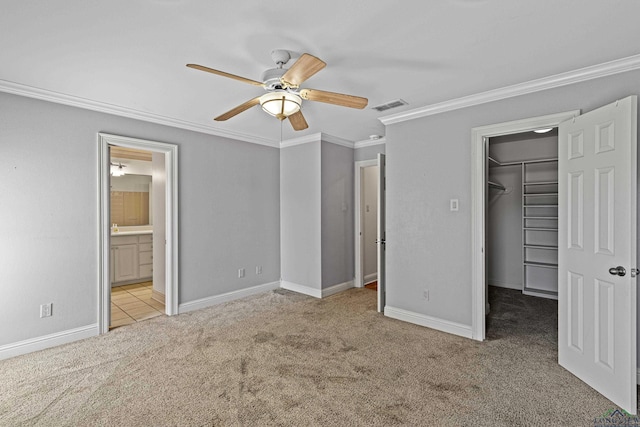 unfurnished bedroom featuring a walk in closet, light carpet, a closet, ornamental molding, and ceiling fan