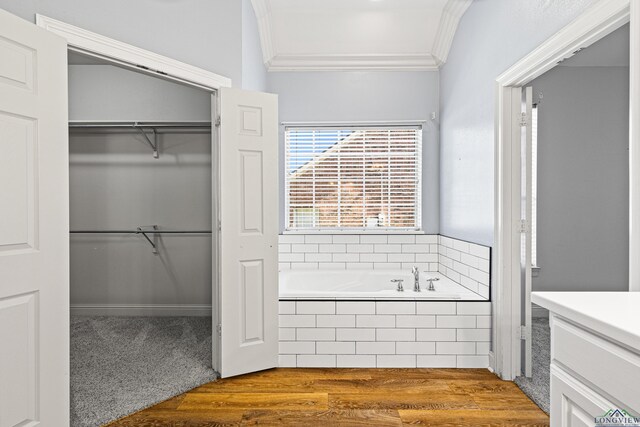 bathroom with wood-type flooring, crown molding, and tiled tub