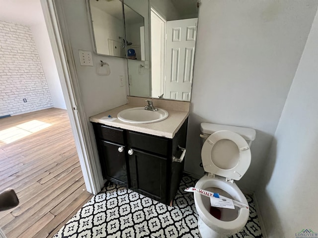 bathroom with hardwood / wood-style flooring, vanity, brick wall, and toilet