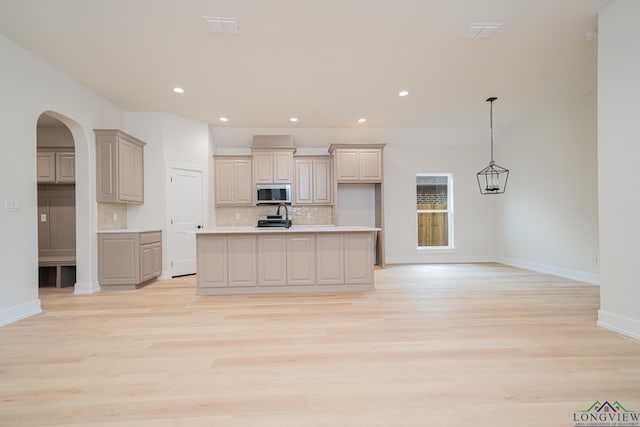 kitchen with decorative backsplash, a center island with sink, pendant lighting, and light hardwood / wood-style flooring