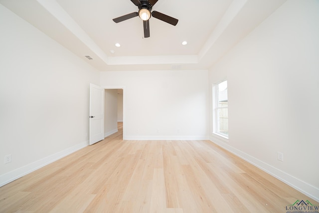 empty room featuring ceiling fan, light wood-type flooring, and a tray ceiling