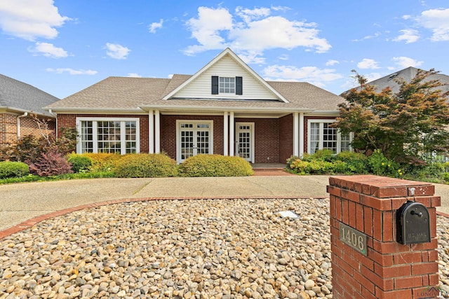 view of front of house featuring a shingled roof, brick siding, and a porch