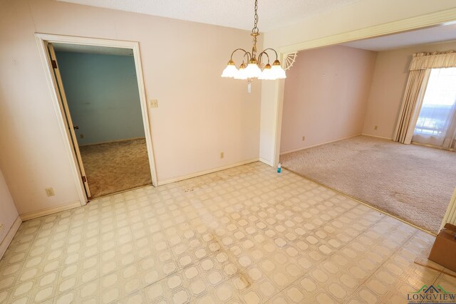 empty room with light colored carpet and a notable chandelier