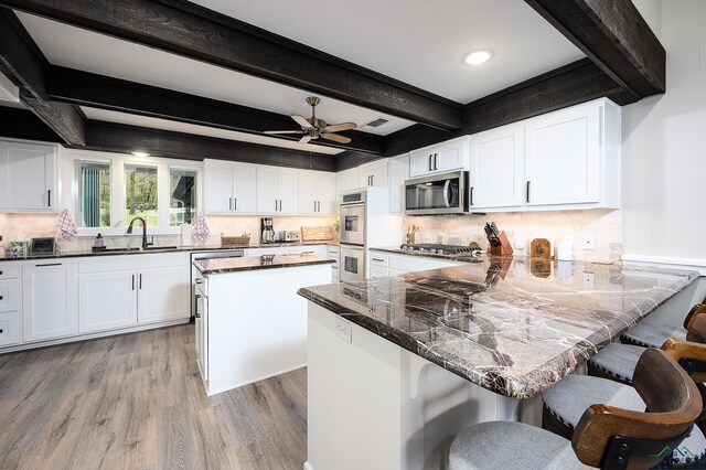 kitchen featuring sink, stainless steel appliances, a kitchen breakfast bar, beamed ceiling, and white cabinets