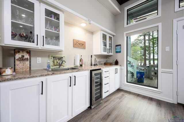 bar featuring wine cooler, light stone countertops, sink, and white cabinets