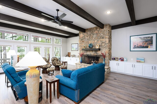 living room with beam ceiling, ceiling fan, french doors, a stone fireplace, and light wood-type flooring