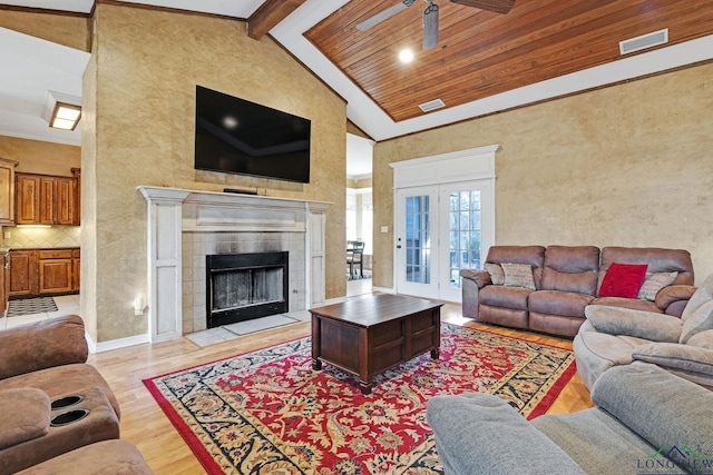 living room featuring light wood-type flooring, a tiled fireplace, french doors, high vaulted ceiling, and beamed ceiling