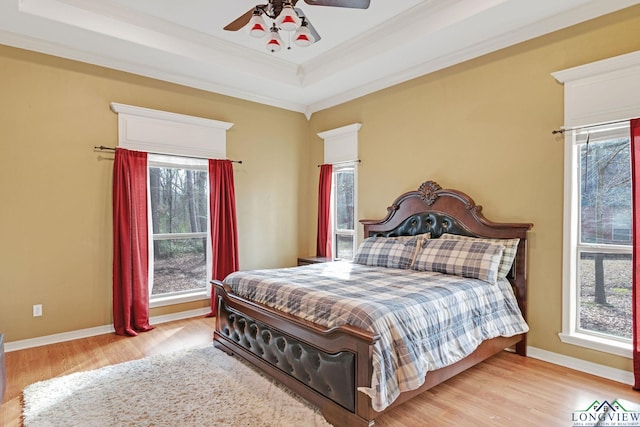 bedroom with multiple windows, a tray ceiling, and light wood-type flooring