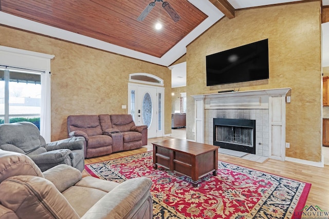 living room featuring light hardwood / wood-style flooring, beamed ceiling, a tile fireplace, ceiling fan, and high vaulted ceiling