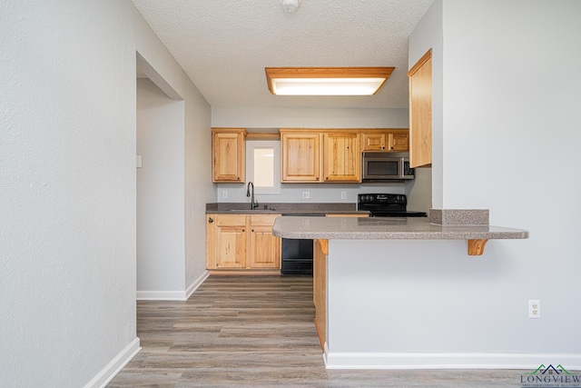 kitchen with light brown cabinets, dishwasher, black / electric stove, a breakfast bar, and sink