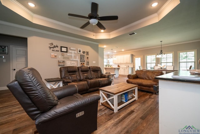 living room with dark wood-type flooring, a tray ceiling, ceiling fan with notable chandelier, and crown molding