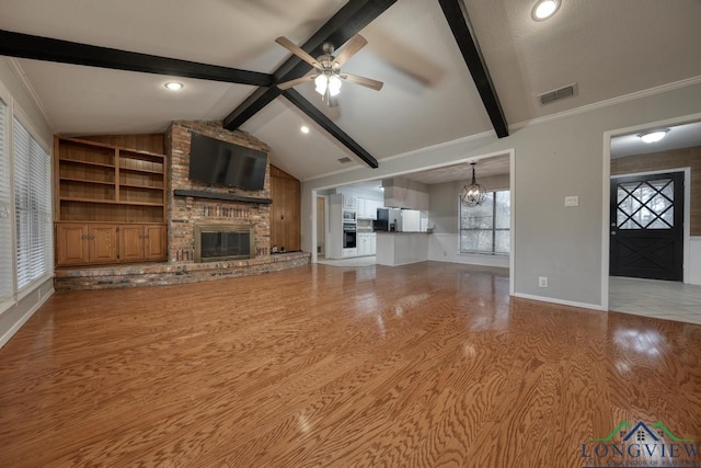 unfurnished living room featuring ceiling fan with notable chandelier, a fireplace, light hardwood / wood-style floors, ornamental molding, and lofted ceiling with beams