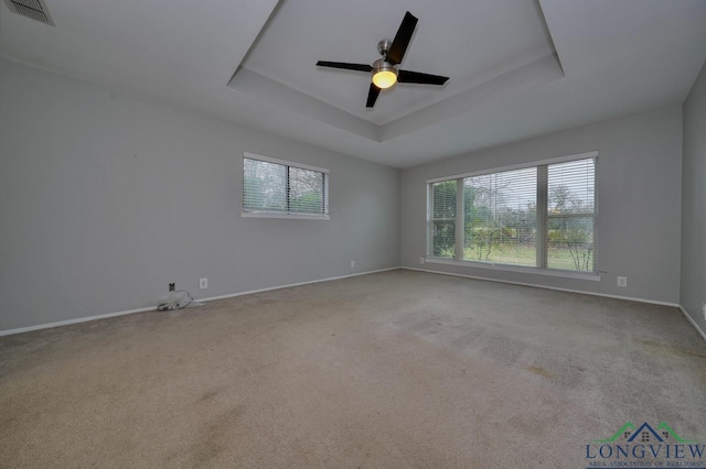 spare room featuring ceiling fan, a tray ceiling, and light carpet