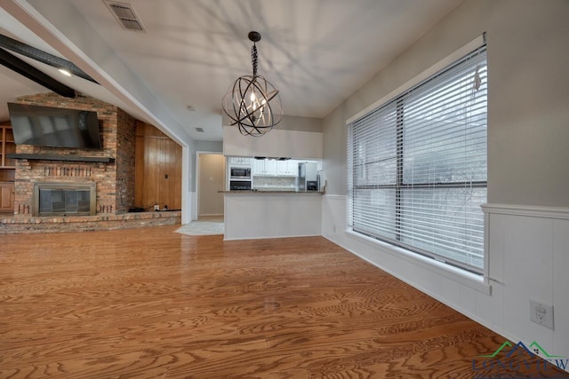 unfurnished living room featuring a brick fireplace, light hardwood / wood-style flooring, and an inviting chandelier