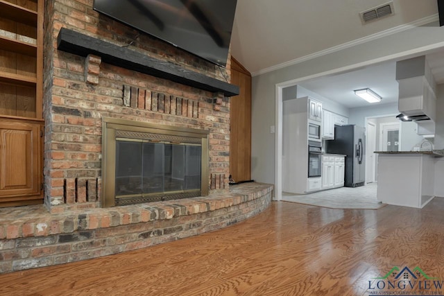 unfurnished living room featuring light wood-type flooring, ornamental molding, lofted ceiling, and a fireplace