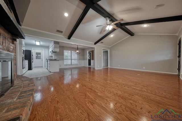 unfurnished living room with light wood-type flooring, ceiling fan, vaulted ceiling with beams, and a brick fireplace