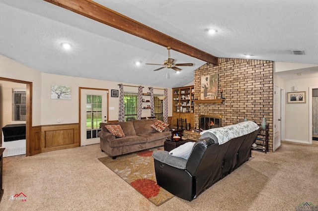 living room featuring wood walls, light carpet, ceiling fan, a fireplace, and a textured ceiling