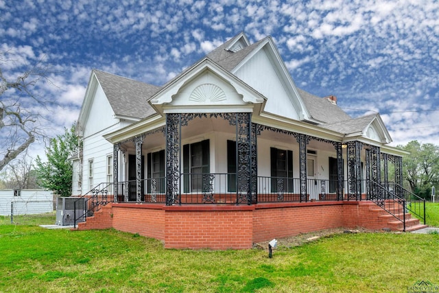 view of front facade with a front lawn, roof with shingles, and a porch