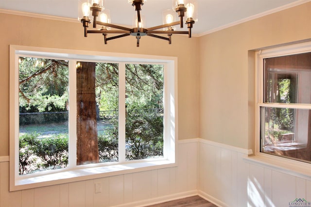 unfurnished dining area featuring ornamental molding, wainscoting, a notable chandelier, and wood finished floors