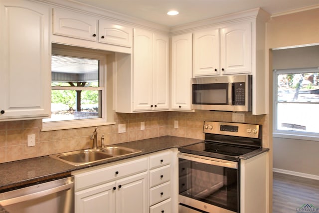 kitchen with dark countertops, appliances with stainless steel finishes, white cabinetry, a sink, and plenty of natural light