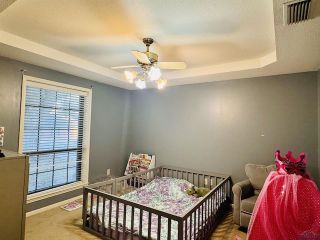 carpeted bedroom with a raised ceiling and ceiling fan