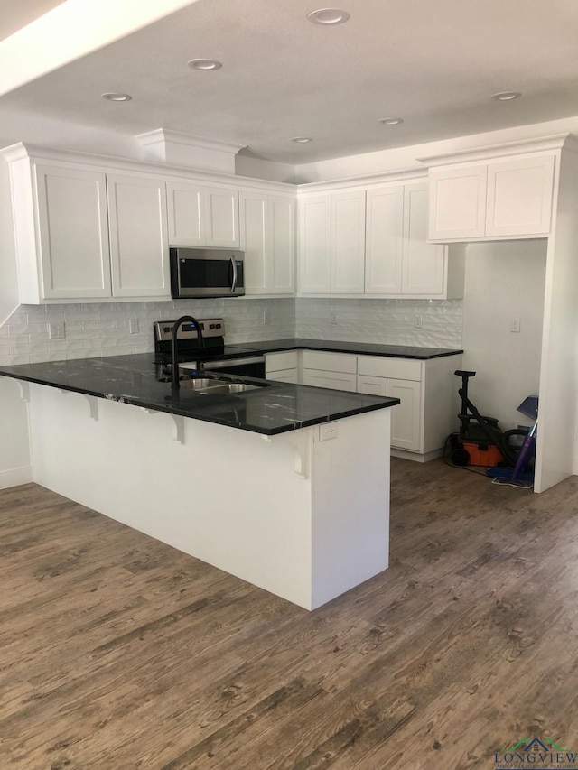 kitchen featuring kitchen peninsula, a breakfast bar, stainless steel appliances, white cabinets, and dark hardwood / wood-style floors