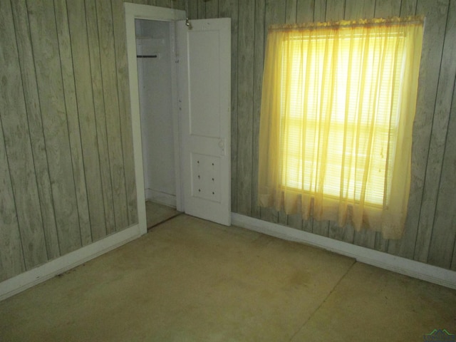 unfurnished bedroom with multiple windows, wood walls, and a closet