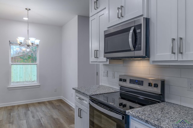 kitchen with pendant lighting, white cabinets, light stone countertops, appliances with stainless steel finishes, and a chandelier