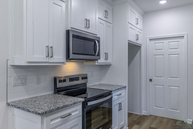 kitchen with decorative backsplash, appliances with stainless steel finishes, light stone counters, hardwood / wood-style flooring, and white cabinets